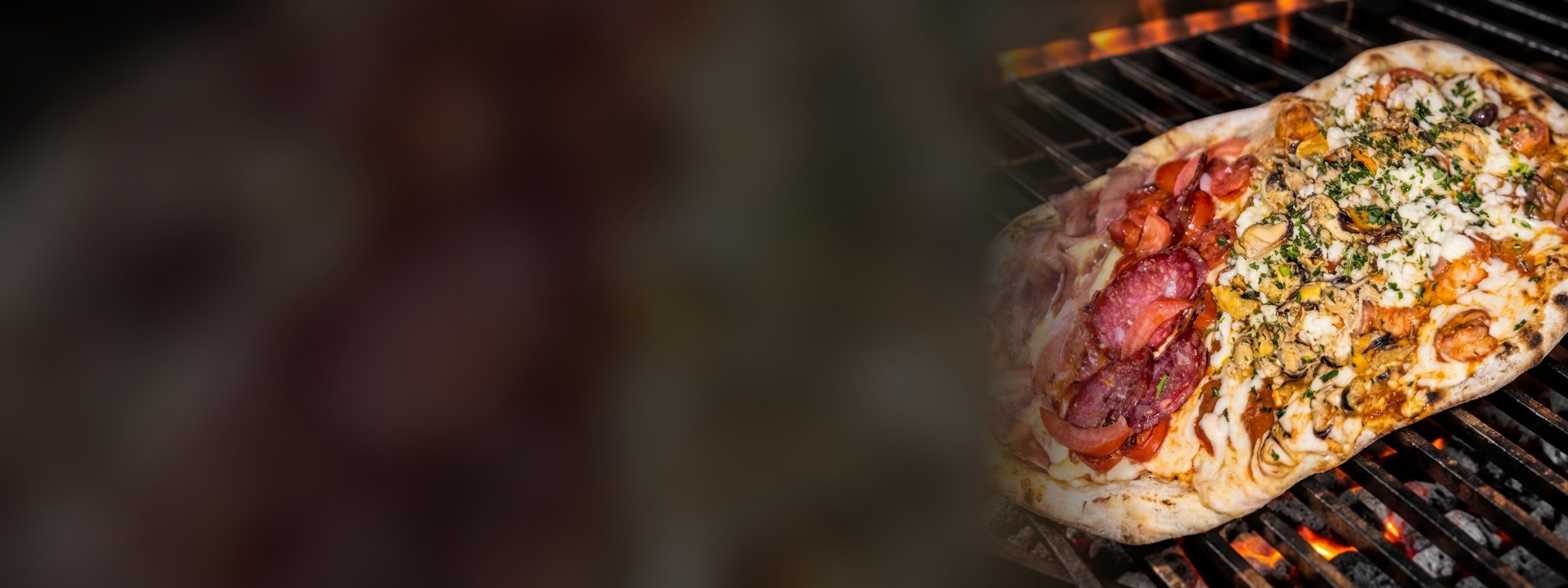 Pizza a la parrilla de Medio Perro, mitad con salame y mitad con hongos, sobre las brasas